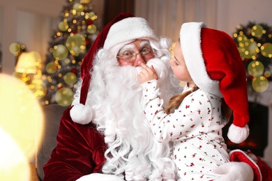 Photo of Santa Claus and cute little girl in room decorated for Christmas