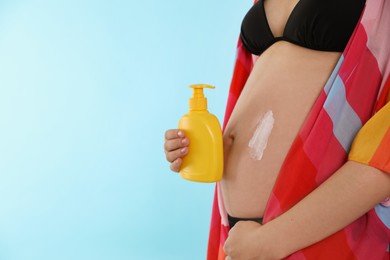 Photo of Young pregnant woman with sun protection cream on light blue background, closeup. Space for text