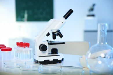 Photo of Professional microscope and glassware on table in chemistry laboratory