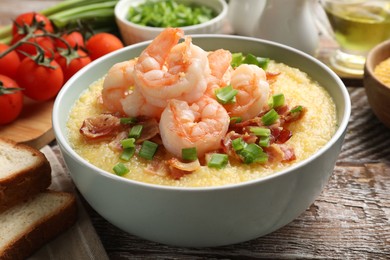 Photo of Fresh tasty shrimps, bacon, grits and green onion in bowl on wooden table, closeup