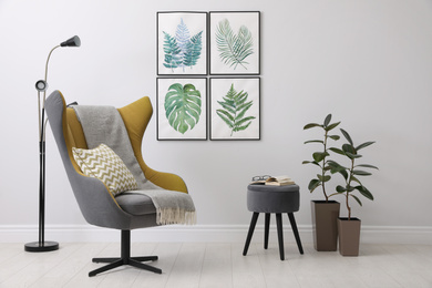 Photo of Stylish room interior with comfortable armchair and paintings of tropical leaves