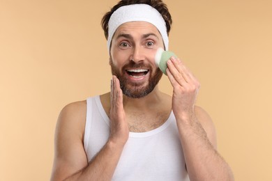 Photo of Man with headband washing his face using sponge on beige background