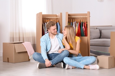 Photo of Happy young couple sitting near wardrobe boxes indoors