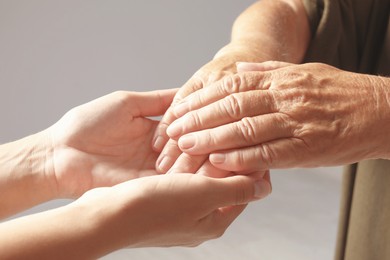 Image of Helping hands on grey background, closeup. Elderly care concept
