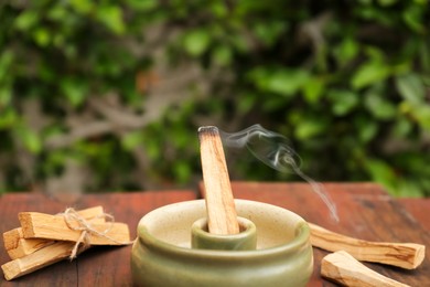 Photo of Palo Santo stick smoldering in holder on wooden table outdoors