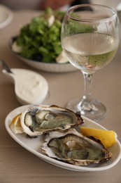 Photo of Plate of delicious raw oysters served with lemon and wine at wooden table