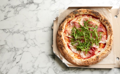Photo of Tasty pizza with meat and arugula in cardboard box on white marble table, top view