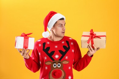 Photo of Surprised handsome man in Santa hat holding gift boxes on yellow background