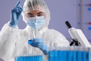 Photo of Scientist taking sample of light blue liquid in laboratory