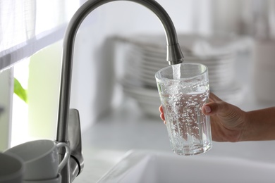 Photo of Woman pouring water into glass in kitchen, closeup