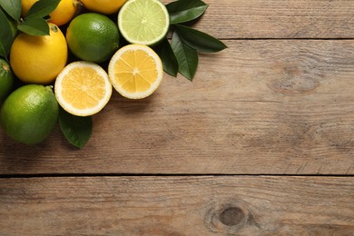 Photo of Fresh ripe lemons, limes and green leaves on wooden background, flat lay. Space for text
