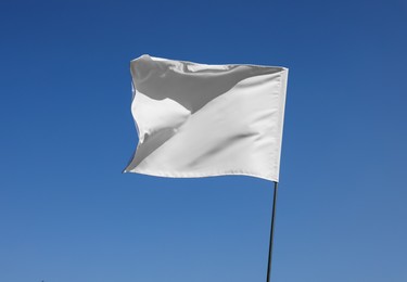 Photo of White flag fluttering against blue sky on sunny day