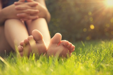 Photo of Teenage girl sitting barefoot on green grass outdoors, closeup. Space for text