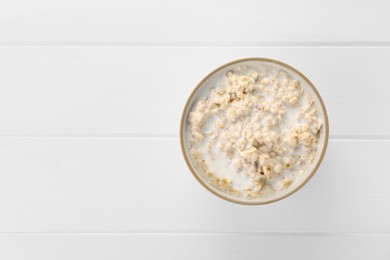 Photo of Tasty boiled oatmeal in bowl on white wooden table, top view. Space for text