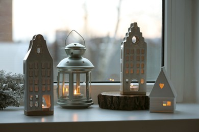 Photo of Beautiful house shaped candle holders and Christmas decor on windowsill indoors
