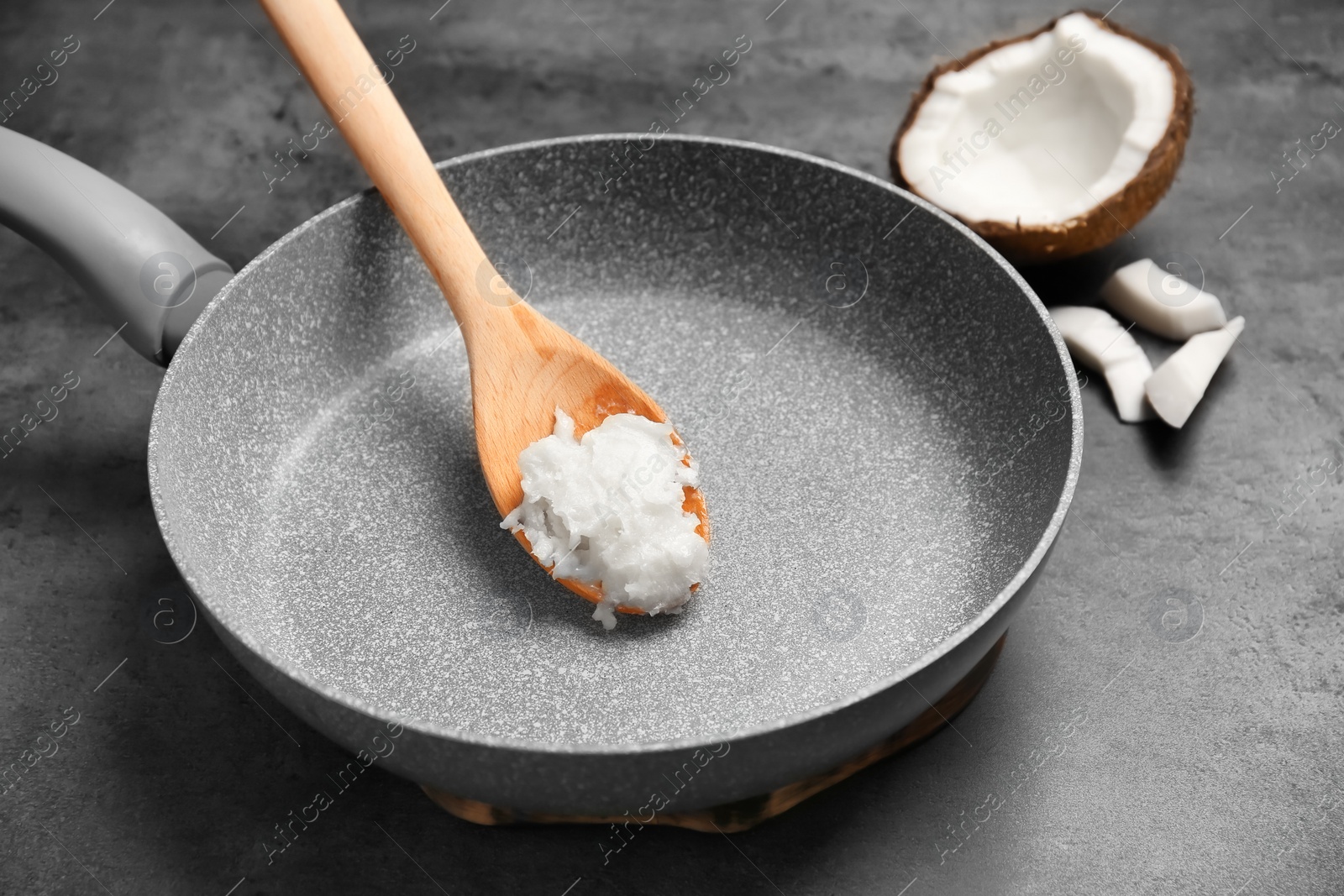 Photo of Frying pan with coconut oil and nut pieces on grey background