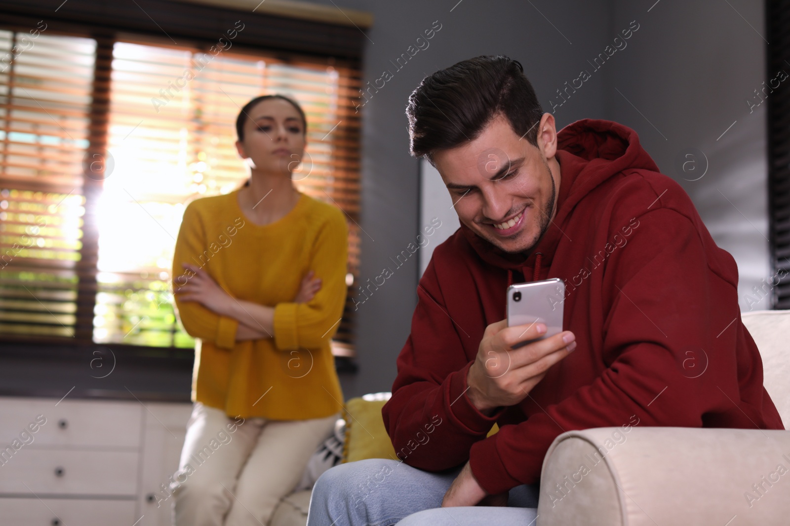 Photo of Distrustful woman peering into boyfriend's smartphone at home. Jealousy in relationship