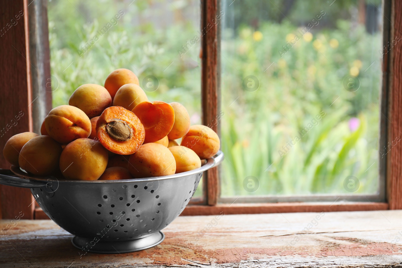 Photo of Colander with delicious ripe apricots on wooden table near window. Space for text