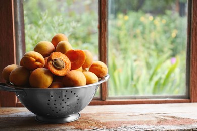 Photo of Colander with delicious ripe apricots on wooden table near window. Space for text
