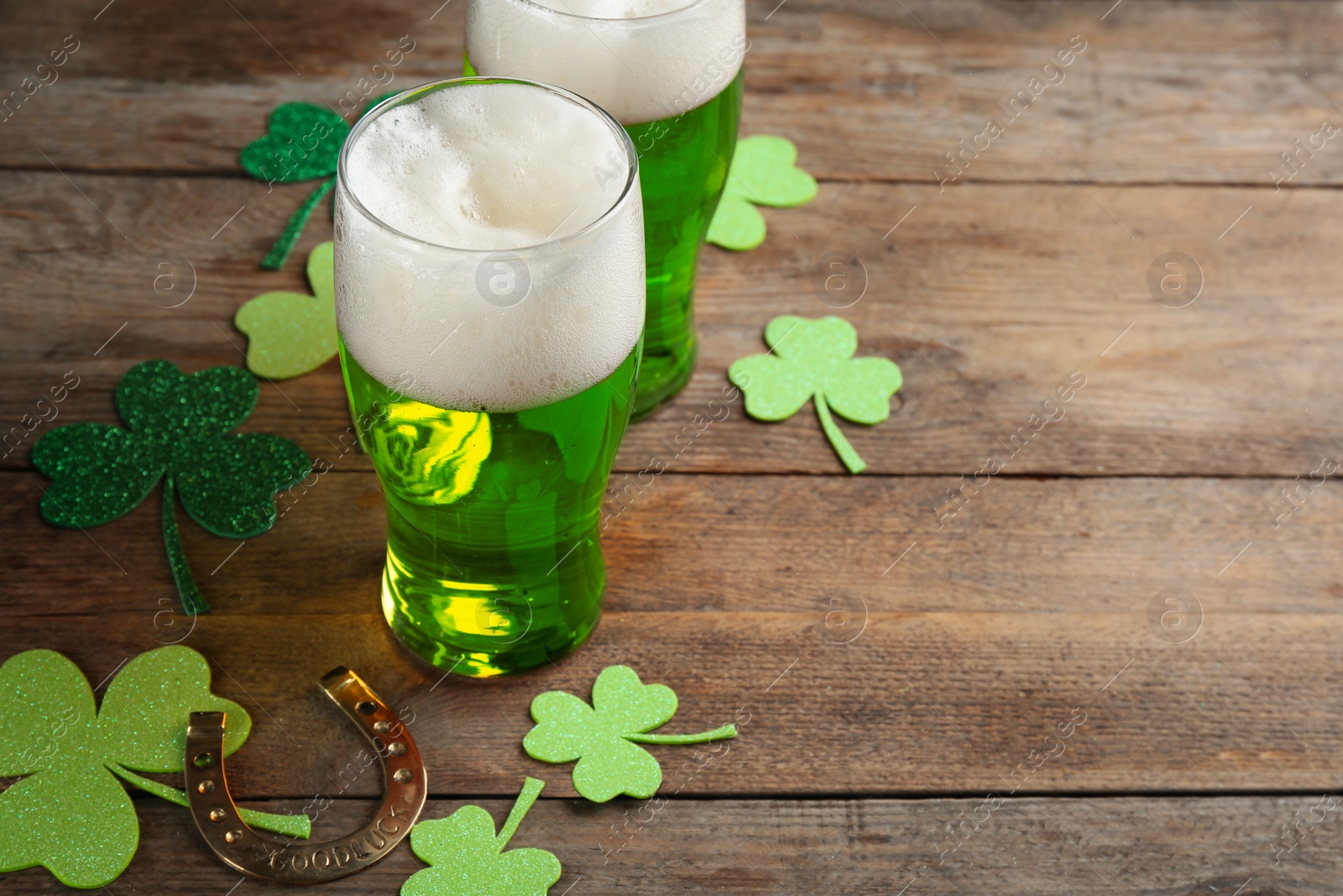 Photo of Green beer, horseshoe and clover leaves on wooden table, space for text. St. Patrick's Day celebration