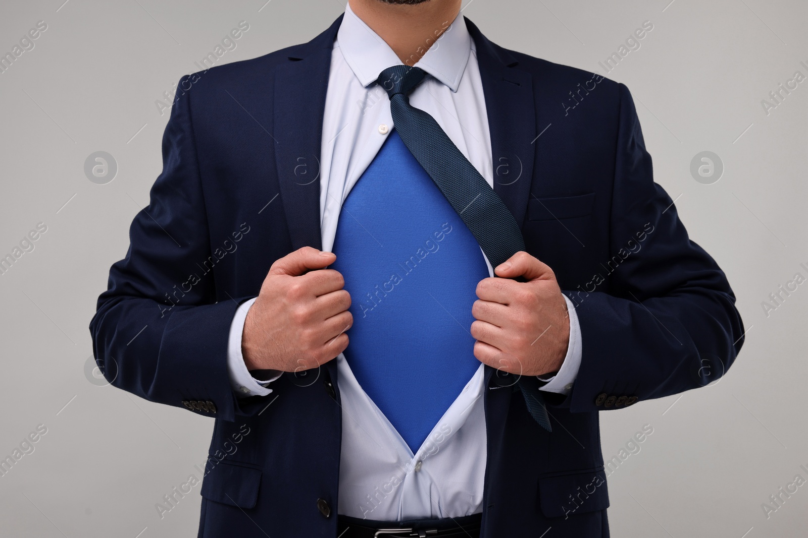 Photo of Businessman wearing superhero costume under suit on beige background, closeup