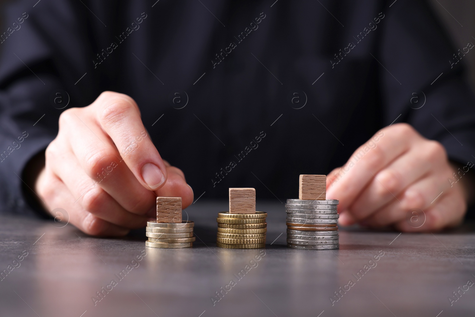 Photo of Taxes. Woman with wooden cubes and coins at grey table, closeup