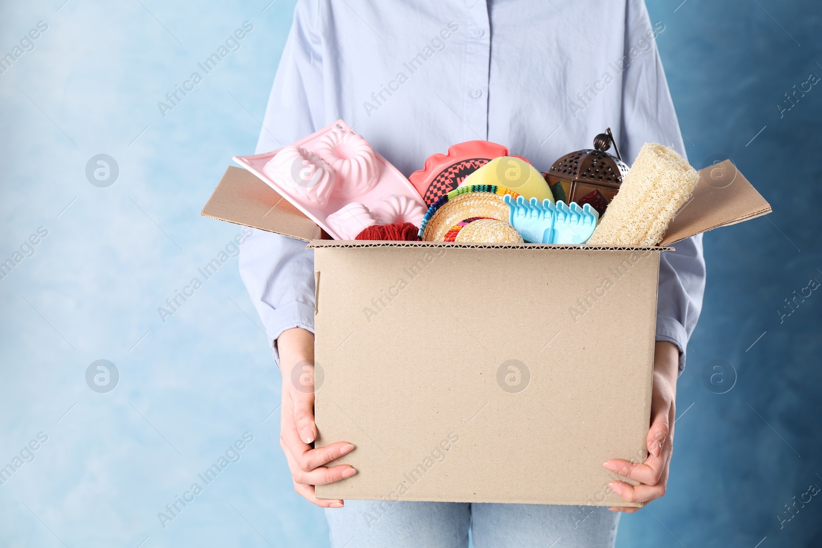 Photo of Woman holding box of unwanted stuff on blue background, closeup. Space for text