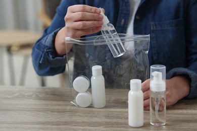 Woman packing cosmetic travel kit at wooden table indoors, closeup. Bath accessories