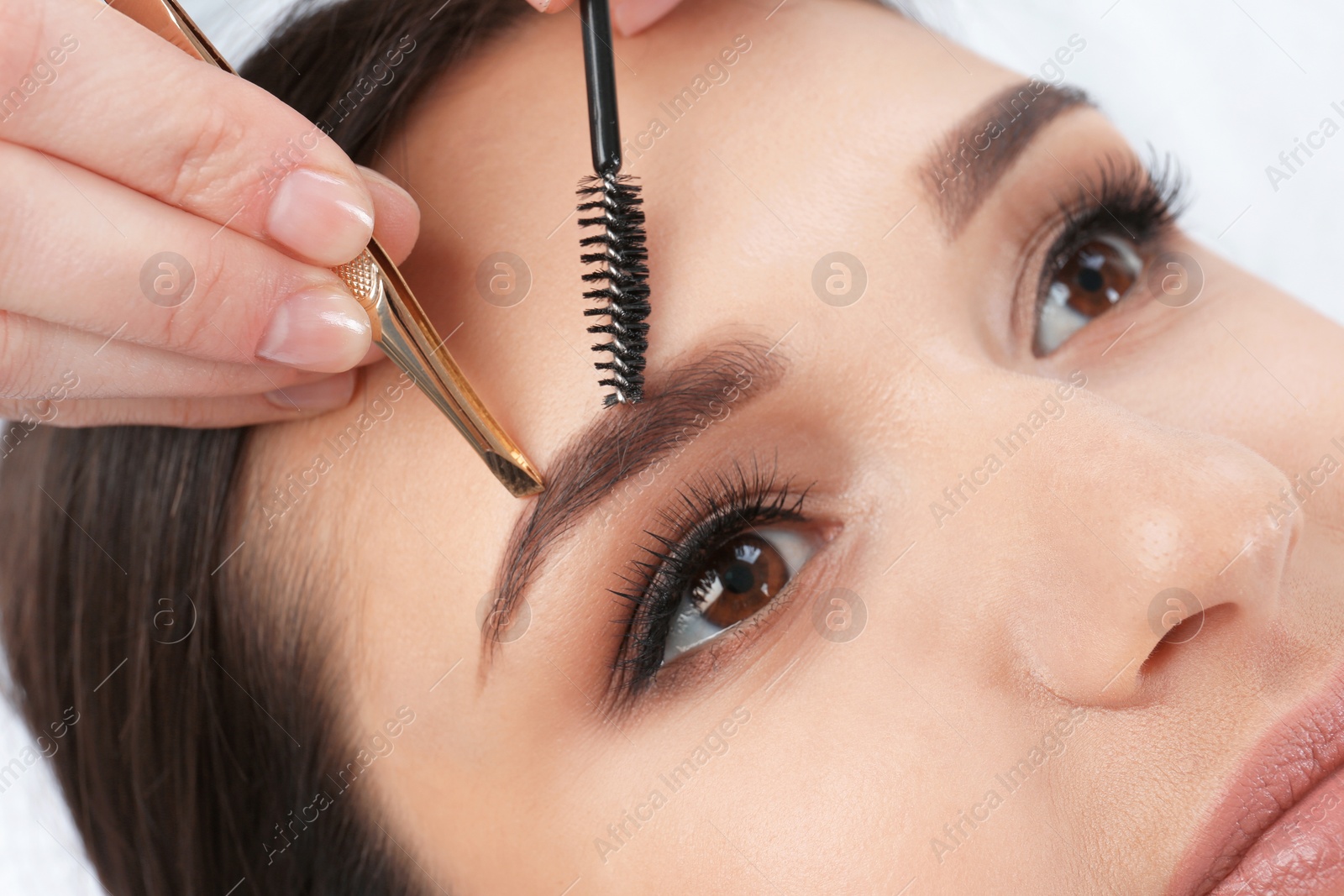 Photo of Young woman having professional eyebrow correction procedure in beauty salon