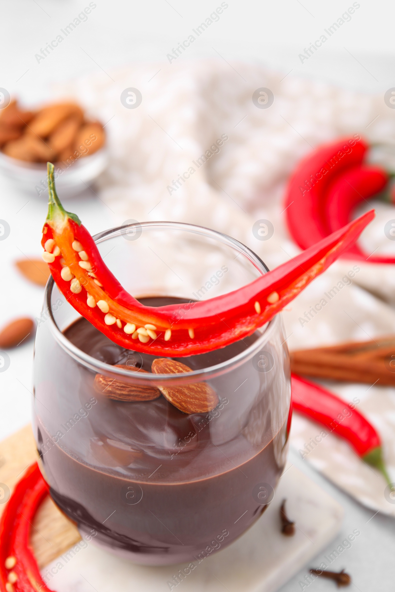 Photo of Glass of hot chocolate with chili pepper and almonds on white table, closeup