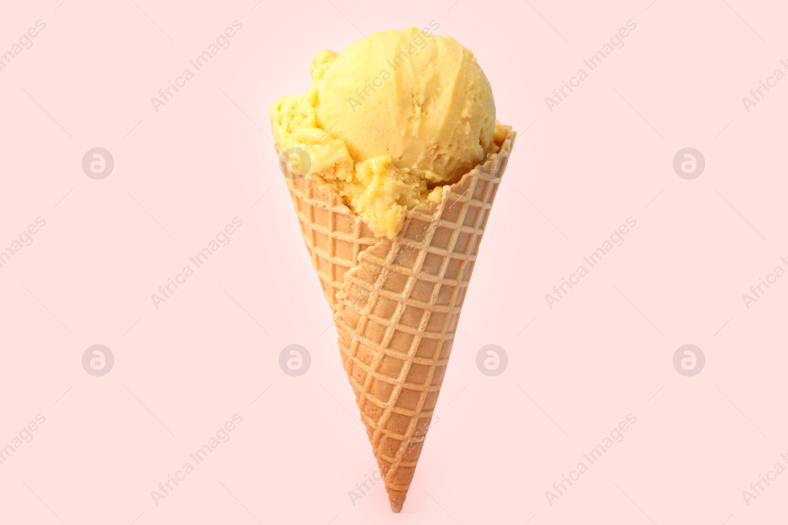 Photo of Delicious yellow ice cream in waffle cone on pink background