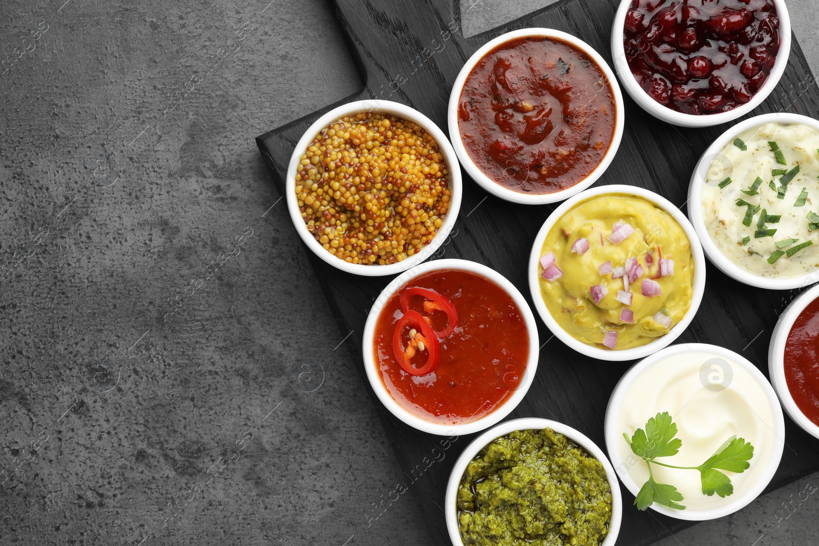 Photo of Different tasty sauces in bowls on grey table, top view. Space for text