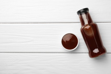 Photo of Tasty barbeque sauce in bottle and bowl on white wooden table, top view. Space for text