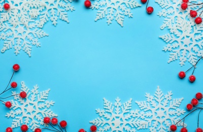 Beautiful decorative snowflakes and red berries on light blue background, flat lay. Space for text