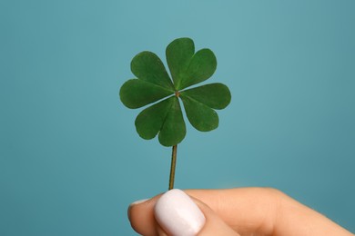 Woman holding green four leaf clover on light blue background, closeup