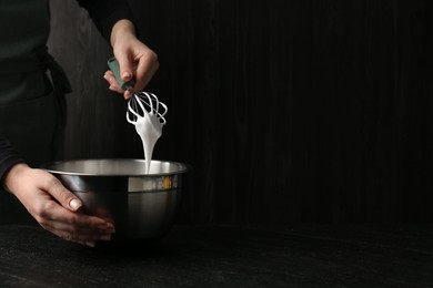 Photo of Woman making whipped cream with whisk at black table, closeup. Space for text