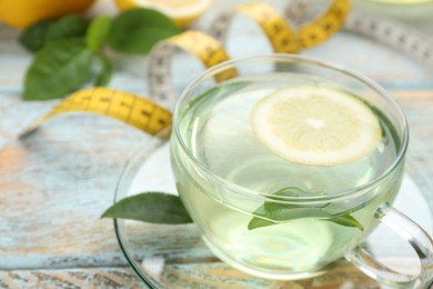 Photo of Glass cup of diet herbal tea with green leaves and lemon on wooden table, closeup