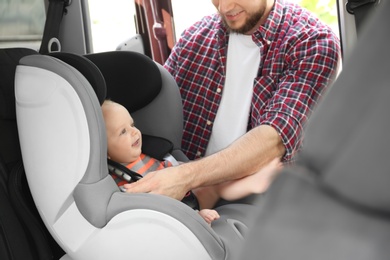 Father fastening baby to child safety seat inside of car