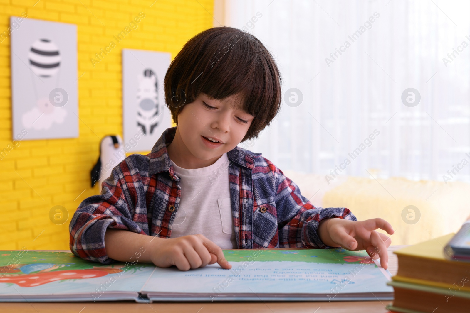 Photo of Cute little boy reading book at table in room