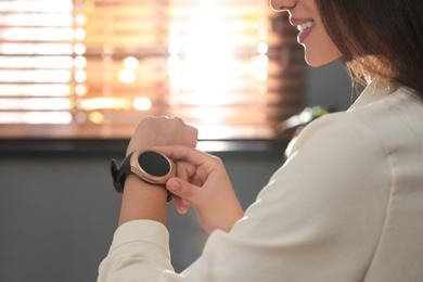 Woman using modern smart watch in office, closeup