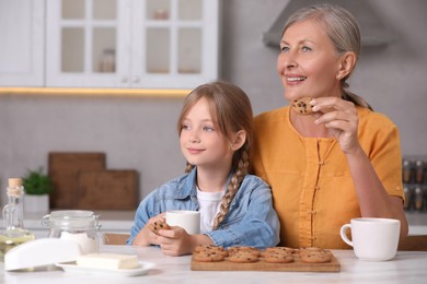 Photo of Happy grandmother with her granddaughter eating cookies in kitchen