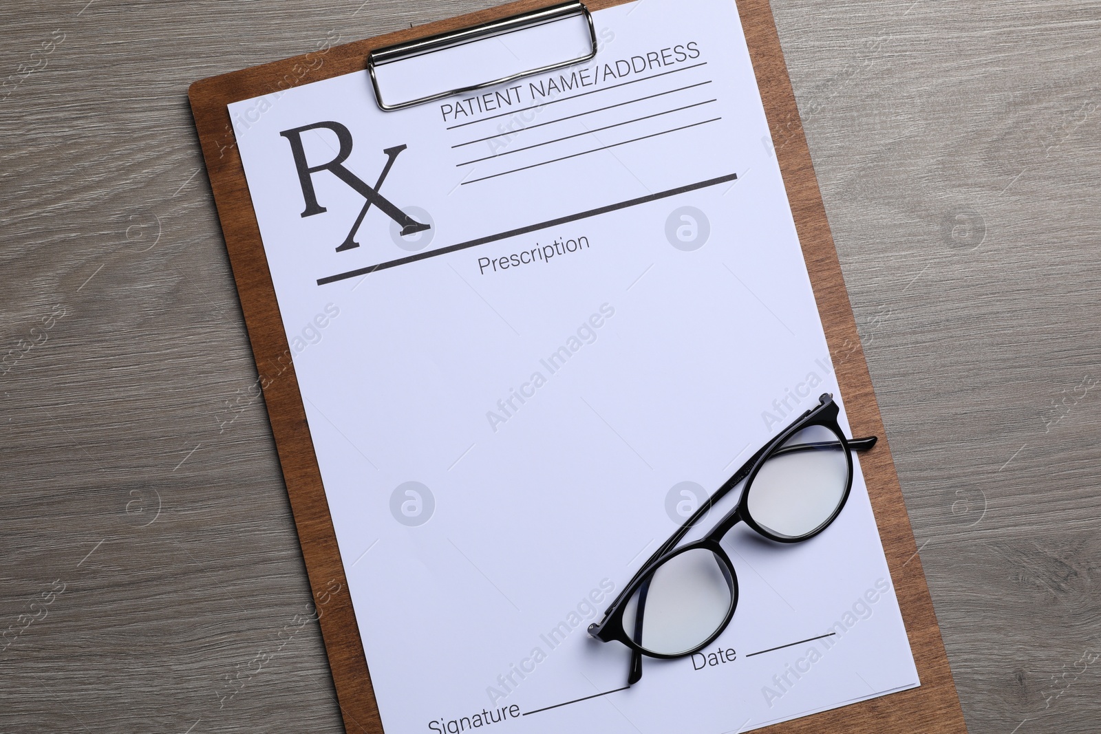 Photo of Clipboard with medical prescription form and glasses on wooden table, top view