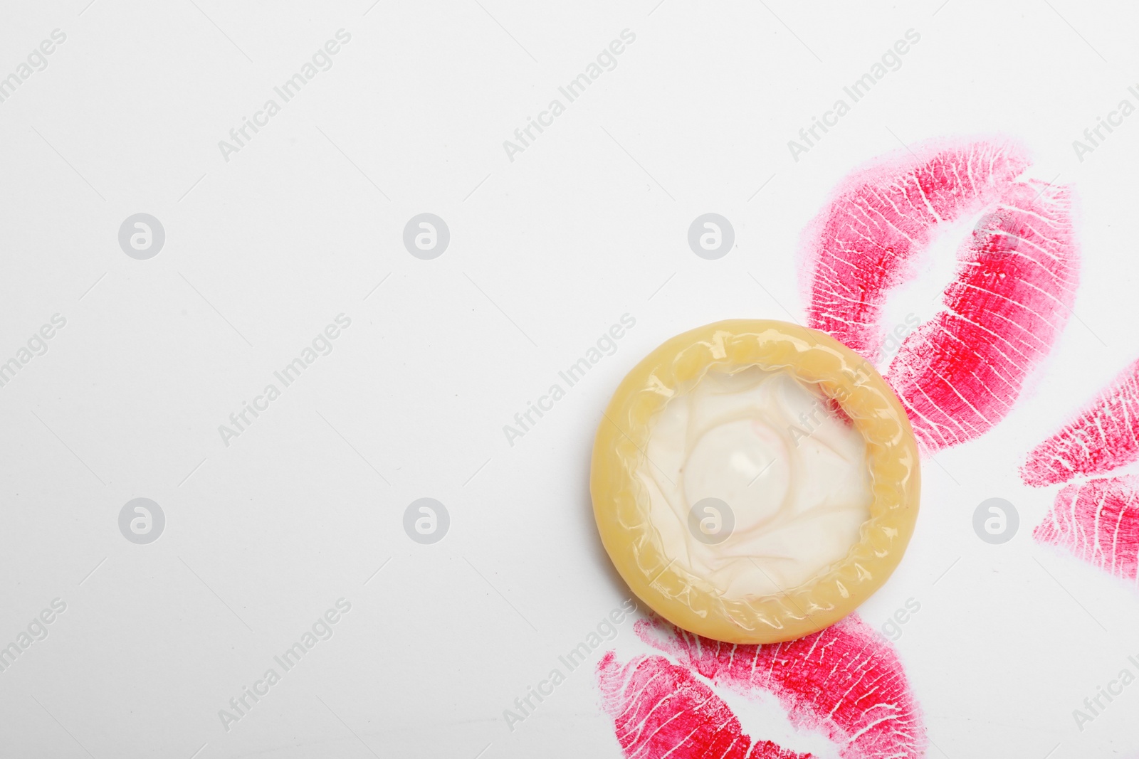 Photo of Condom and lipstick kiss marks on white background, top view. Safe sex