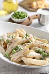 Delicious pasta with green peas and creamy sauce in bowl on table