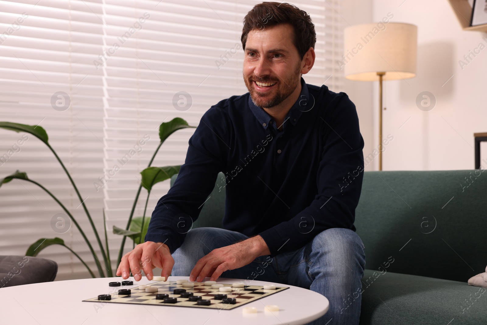 Photo of Happy man playing checkers on sofa at home