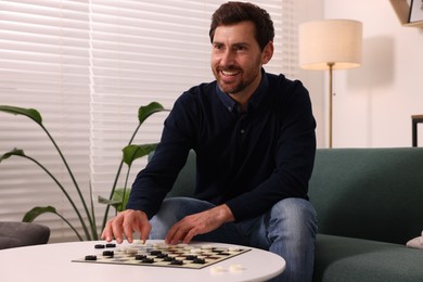 Happy man playing checkers on sofa at home