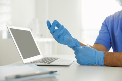 Doctor putting on medical gloves at table in office, closeup