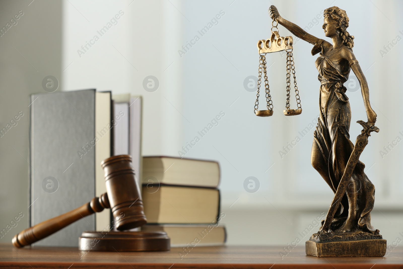 Photo of Figure of Lady Justice, gavel and books on wooden table indoors. Symbol of fair treatment under law