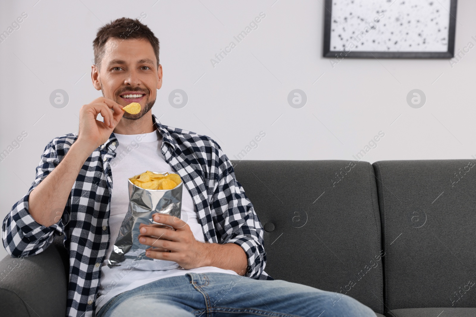 Photo of Handsome man eating potato chips on sofa at home