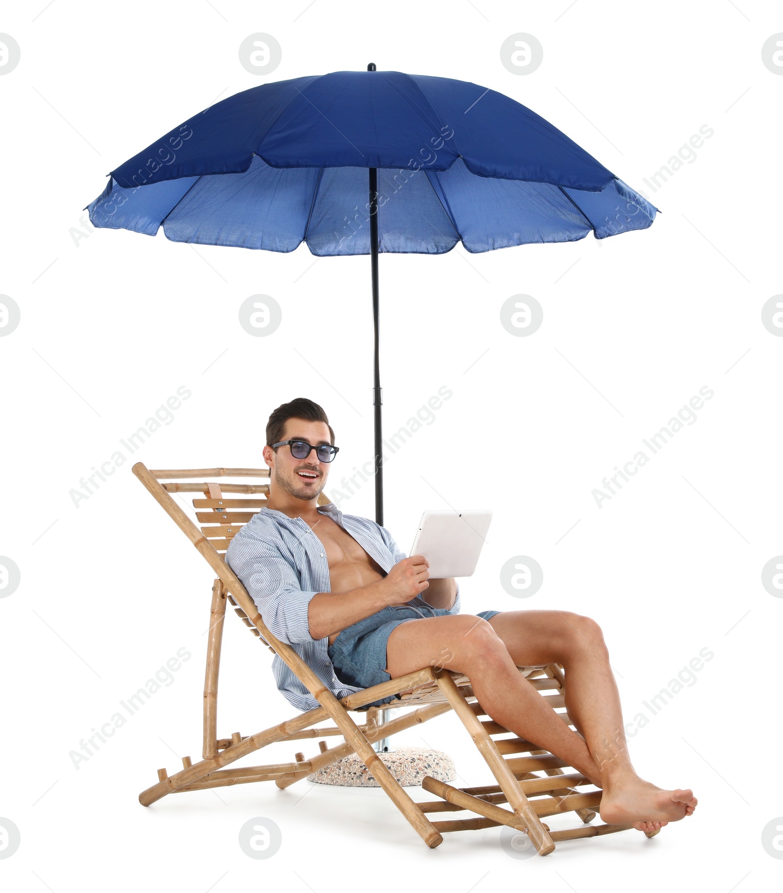 Photo of Young man with tablet on sun lounger under umbrella against white background. Beach accessories